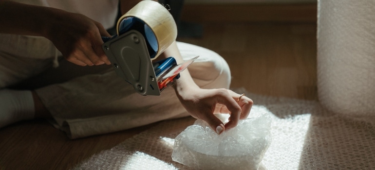 person wrapping items in bubble wrap as that is included in room by room packing guide