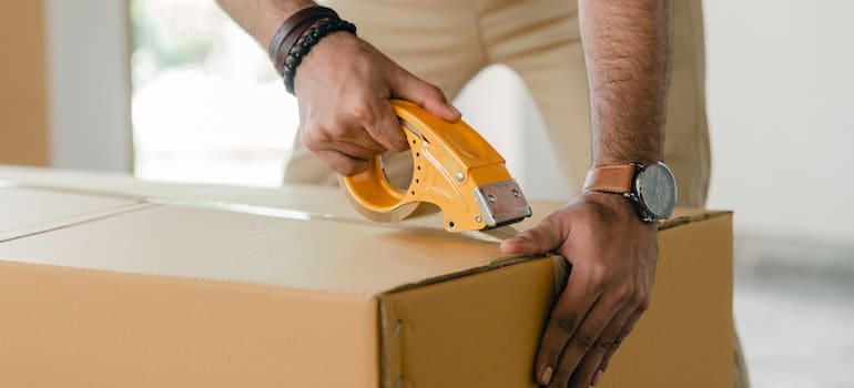 man taping carrying box with scotch