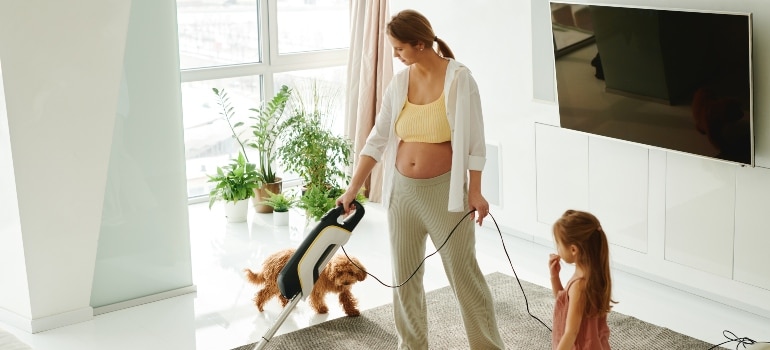 pregnant woman vacuuming as an example that safely moving while pregnant shouldn't include heavy tasks