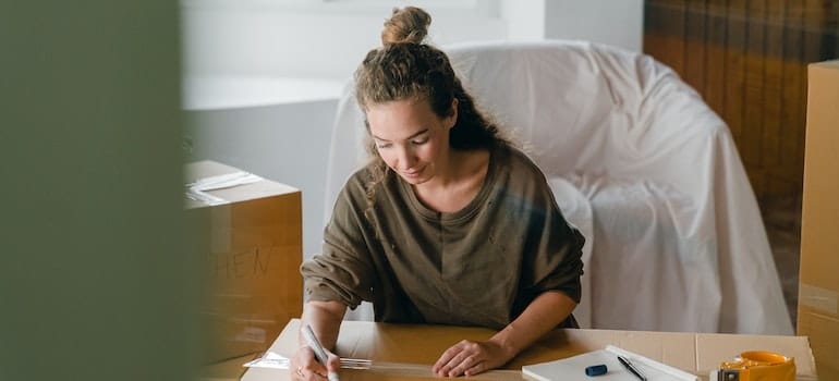 Woman signing box with a marker while sitting in the living room.