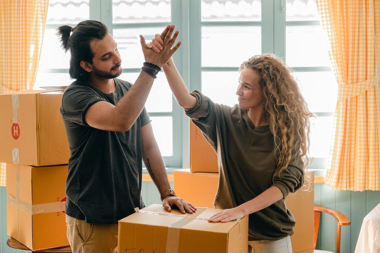 Picture of a couple giving high five next to a pile of cardboard boxes