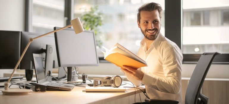smiling man holding a book and sitting at his office desk